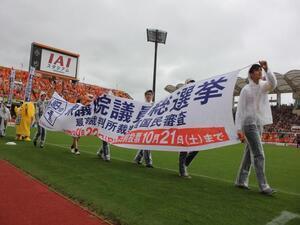 写真：横断幕を持ちサッカー場を歩く啓発活動の様子